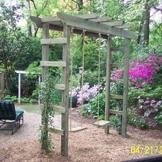 a wooden swing set sitting in the middle of a garden with purple flowers around it