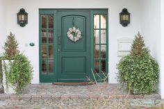 a green front door with two wreaths on it and some plants in the foreground