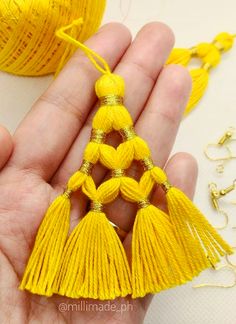 a person holding a yellow tassel in their hand next to some balls of thread