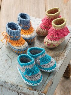 several pairs of crocheted baby shoes sitting on top of a piece of wood