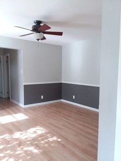 an empty room with hard wood flooring and fan in the corner, painted gray and white