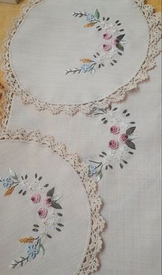 three white doily with flowers on them sitting on top of a wooden tablecloth