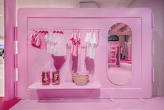 a pink room with clothes hanging on the wall and a mirror in the corner behind it