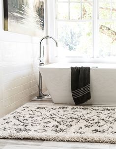 a bath tub sitting next to a window on top of a white rug in a bathroom