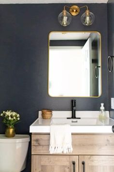 a white toilet sitting next to a bathroom sink under a mirror above a wooden cabinet