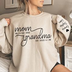 a woman sitting on top of a bed wearing a sweatshirt that says mom grandma est 1932