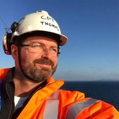 a man in an orange safety vest and hard hat on a boat looking at the camera