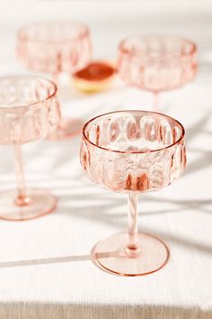 three pink wine glasses sitting on top of a white table cloth next to each other