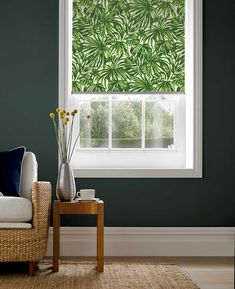 a living room with green walls and a window covered in leafy blinds on the windowsill