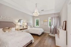 two beds in a bedroom with white walls and wood floors, one has a chandelier