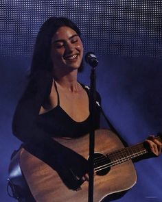 a woman holding a guitar and singing into a microphone