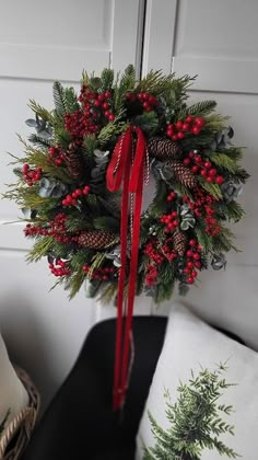 a christmas wreath hanging on the front door with red berries, pine cones and evergreens