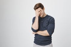 a young man is holding his hand to his face while standing against a white background