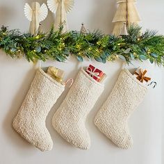 three christmas stockings hanging from a mantel decorated with greenery and bows, along with other holiday decorations