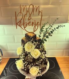 a cake with white flowers and greenery sits on top of a stovetop in front of a brick wall