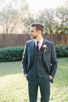 a man in a suit and tie standing in the grass with his hands in his pockets