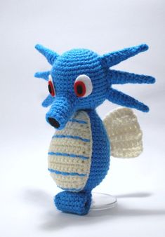 a crocheted blue and white stuffed animal with red eyes holding a piece of bread