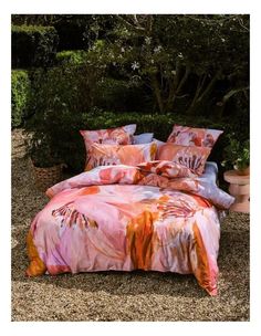 a bed covered in pink and orange comforter next to a bush filled with trees