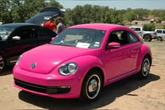 a pink volkswagen beetle parked next to other cars