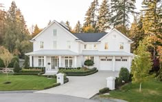 a large white house surrounded by lush green trees and bushes in front of it,