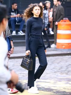 a woman in black is walking down the street with her hand on her hip bag