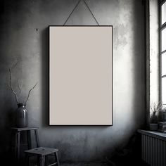 an empty frame hanging on the wall next to a chair and window in a dark room