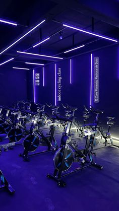 there are many exercise bikes in the gym with neon lights on the wall behind them