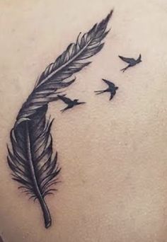 a woman's back with a black feather and birds flying around her tattoo design