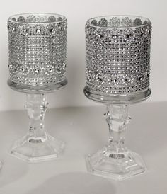 two crystal candlesticks sitting side by side on a white surface with one candle in the middle