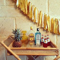 there is a tray with bottles and pineapples on it next to a string of yellow streamers