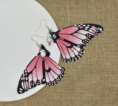 two pink and black butterfly earrings on a white plate with burliegt background