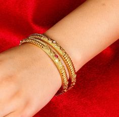 Antique gold-plated bangle from Amrapali is a masterpiece of South Indian jewelry. Known as a Kada bracelet, it features traditional jadau craftsmanship and Kemp stones, making it ideal for temple and bridal wear. This exquisite piece serves as a timeless gift, embodying the rich cultural heritage of India. *𝐏𝐑𝐎𝐃𝐔𝐂𝐓 𝐃𝐄𝐓𝐀𝐈𝐋* * Material: Brass * Plating: Gold Plated *𝐃𝐈𝐌𝐄𝐍𝐒𝐈𝐎𝐍𝐒* * Weight: 15 gm * Width: 0.2 Inches     *𝐃𝐈𝐒𝐂𝐋𝐀𝐈𝐌𝐄𝐑* Product color may slightly vary du Elegant Bangle For Navratri, Temple Jewelry Style Gold Bracelet For Ceremonial Festivals, Temple Jewelry Gold Bracelet For Ceremonial Festivals, Temple Style Gold Bracelet For Ceremonial Festivals, Festival Temple Jewelry 22k Gold Bracelets, Ceremonial Temple Style Gold Bracelet For Festivals, Gold Bollywood Bangle For Navratri, Elegant Bangle Bracelet For Navratri, Elegant Gold Bangle For Navratri