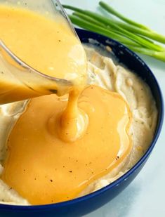 a blue bowl filled with mashed potatoes and gravy being drizzled over