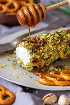 a plate with pretzels, nuts and honey being drizzled over them