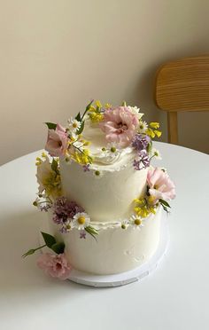 a three tiered white cake with flowers on the top and bottom is sitting on a table