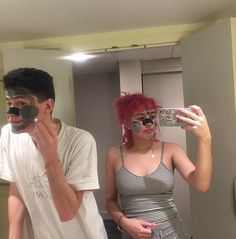 a man and woman with face paint taking a selfie in front of a mirror