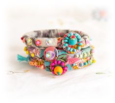 three bracelets with colorful beads and tassels on white fabric background, closeup