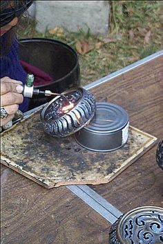 a person is using a lighter to light up some tins on a table outside