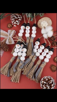 snowman ornaments are displayed on a red surface with pine cones and twine balls