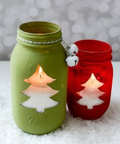 two red and green mason jars with christmas trees painted on them, sitting on snow