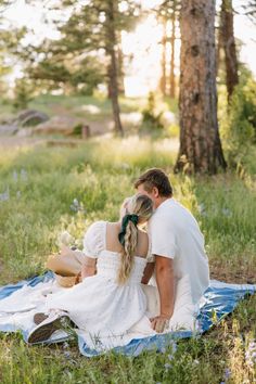 a man and woman are sitting on a blanket in the woods with their backs to each other