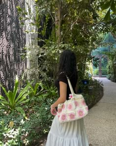 a woman walking down a path carrying a pink and white handbag in her left hand