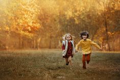 two young children running through a field in the fall with trees and grass behind them