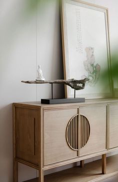 a wooden cabinet with a bird on top and a mirror above it in a white room