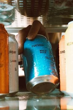 a person is holding a can of soda in front of several other cans on the counter