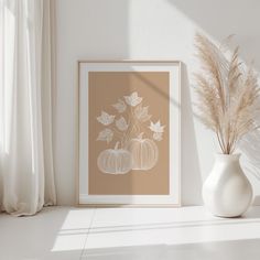 a white vase sitting next to a window filled with flowers and leaves on top of a table