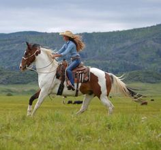 a woman riding on the back of a brown and white horse in a grassy field