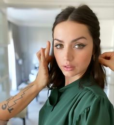 a woman with tattoos on her arm is looking at the camera and touching her hair