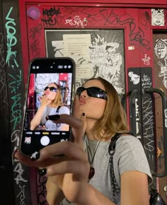 a woman taking a selfie with her cell phone in front of graffiti covered wall