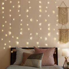 a bed topped with pillows next to a wall covered in string lights